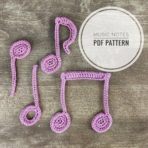 Puede incluir: Cuatro notas musicales de ganchillo de color rosa sobre un fondo de madera marrón. Las notas están dispuestas en línea con el texto "MUSIC NOTES PDF PATTERN" en un círculo blanco encima de ellas.