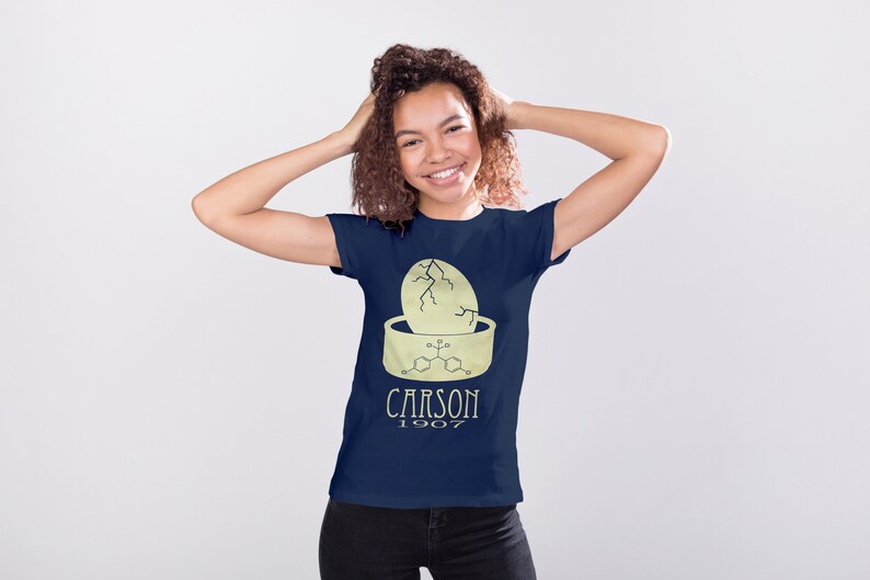 May include: A navy blue t-shirt with a yellow graphic of a cracked egg with a chemical formula and the text "CARSON 1907".