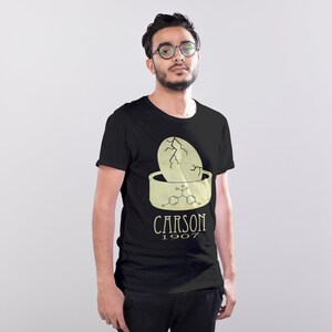 May include: A black t-shirt with a graphic of a cracked egg in a bowl with a chemical formula and the text "CARSON 1907".