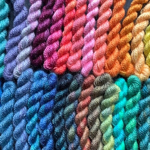 May include: A collection of colorful embroidery floss in various shades, including blues, purples, pinks, oranges, and greens. The floss is tightly wound into small bundles, showcasing a range of hues for crafting projects.