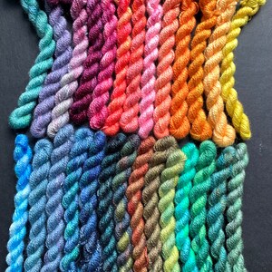 May include: A collection of colorful embroidery floss in a variety of shades, including blues, greens, pinks, oranges, and yellows. The floss is neatly arranged, showcasing the different hues and textures of the threads. The image is taken against a dark background.