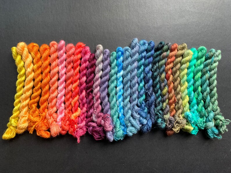 May include: A collection of colorful embroidery floss in a spectrum of hues, from warm yellows and oranges to cool blues and greens. The floss is tightly wound, showcasing a variety of shades for crafting and embroidery projects.