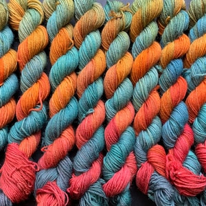 May include: A collection of skeins of yarn in shades of orange, teal, and red. The yarn is arranged in a spiral pattern.