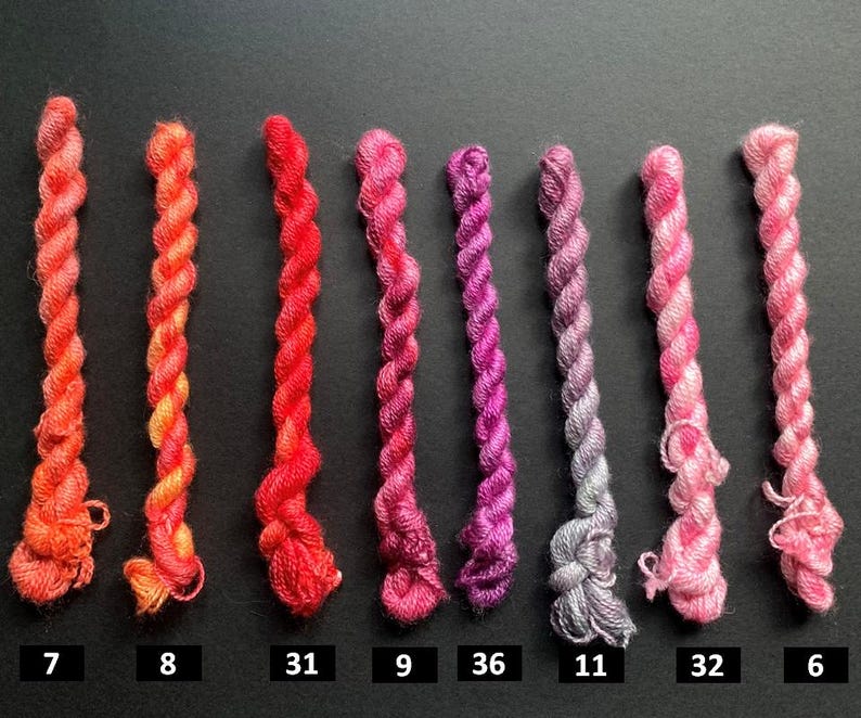 May include: A collection of eight twisted embroidery floss skeins in a gradient of colors from orange to pink. Each skein is labeled with a number, ranging from 6 to 36, against a dark background. Ideal for embroidery and craft projects.