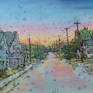 May include: A watercolor painting of a street scene with houses on either side of the road. The sky is a light blue with pink and orange clouds. The houses are painted in shades of blue, green, and brown. There are trees and power lines in the background. The street is empty and the ground is covered in a light layer of rain.