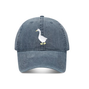 May include: A blue denim baseball cap with a white embroidered goose design.