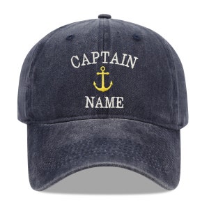 May include: A navy blue baseball cap with the text "CAPTAIN" and an anchor symbol embroidered in yellow. The text "NAME" is embroidered in white below the anchor.