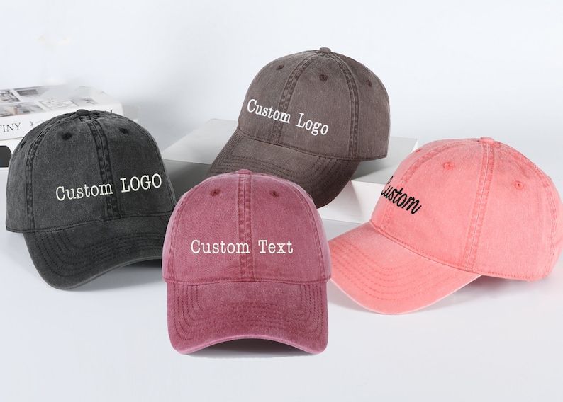May include: Four baseball caps in different colors with customizable text. The caps are gray, black, pink, and red. The text on the caps reads "Custom Logo", "Custom Text", and "Custom".