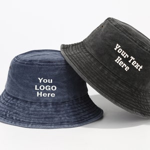 May include: Two bucket hats, one black and one blue, with white embroidered text. The black hat says "Your Text Here" and the blue hat says "You Logo Here".