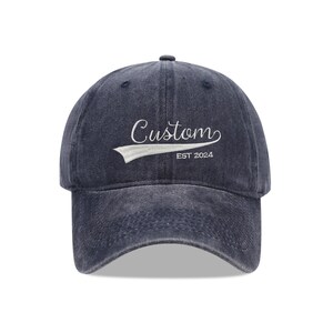 Pode incluir: Um boné de beisebol de denim azul marinho com um logotipo branco bordado que diz "Custom Est 2024".