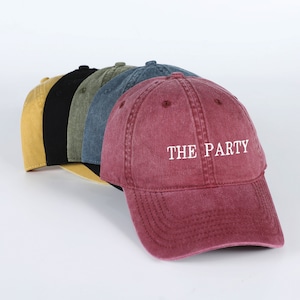 May include: Five baseball caps in different colors, including yellow, black, green, blue, and red. The red cap has the text "THE PARTY" embroidered on the front in white.