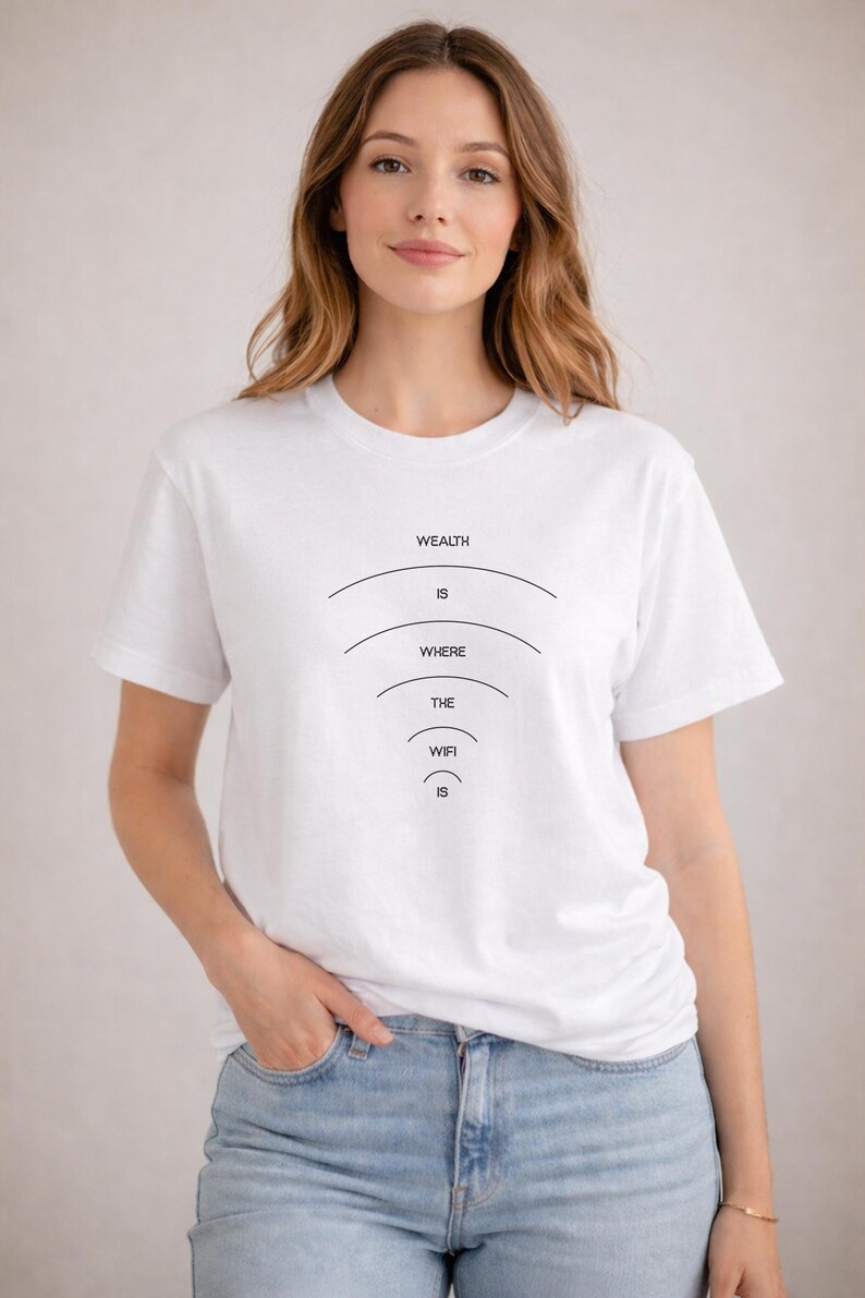 May include: White t-shirt with the text "WEALTH IS WHERE THE WIFI IS" in black. The text is arranged in a descending arc design. The model is wearing blue jeans.