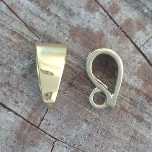 May include: Two gold-toned metal pendant clasps. One clasp is a simple, flat, triangular shape. The other clasp is a teardrop shape with a small loop at the top.
