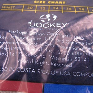 May include: A dark blue plastic packaging material featuring a white size chart for waist measurements 30 through 40. The text includes Jockey International Inc. branding, copyright information from 1996, and a statement regarding assembly in Costa Rica.