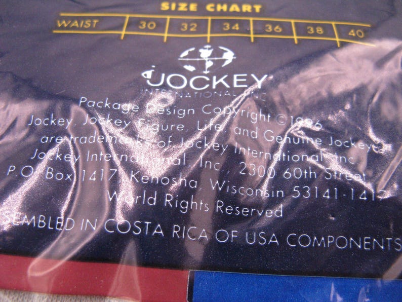 May include: A dark blue plastic packaging material featuring a white size chart for waist measurements 30 through 40. The text includes Jockey International Inc. branding, copyright information from 1996, and a statement regarding assembly in Costa Rica.