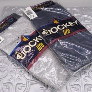 May include: Two packages of Jockey Life brand briefs, one in heather gray and one in navy blue. Each package is sealed in clear plastic and features a dark blue label with the Jockey Life logo, size 38, and text indicating 100% cotton material.