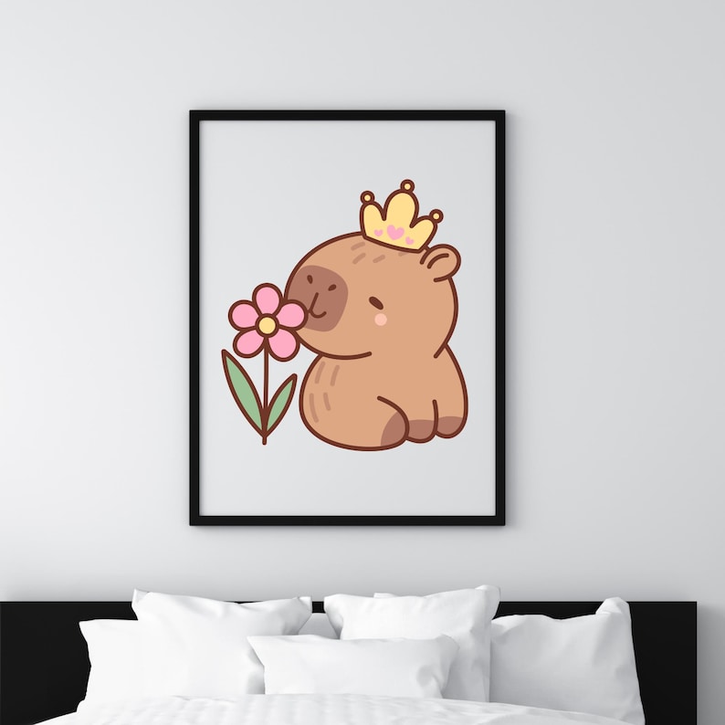 May include: A framed art print featuring a cartoon capybara wearing a gold crown with a pink heart. The capybara is sniffing a pink flower with green leaves. The artwork is set against a white background.