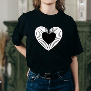 Pu&ograve; includere: Una maglietta nera con una grafica bianca a forma di cuore con cerchi concentrici.
