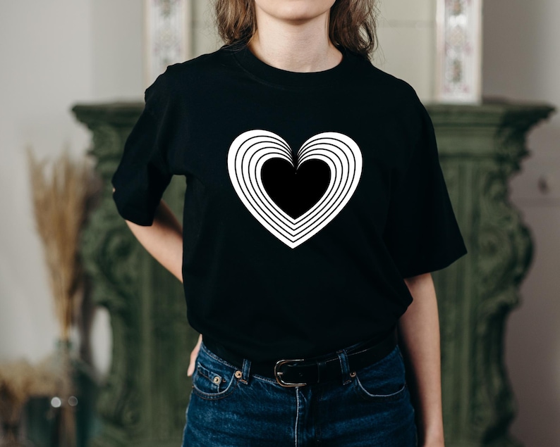 Pu&ograve; includere: Una maglietta nera con una grafica bianca a forma di cuore con cerchi concentrici.