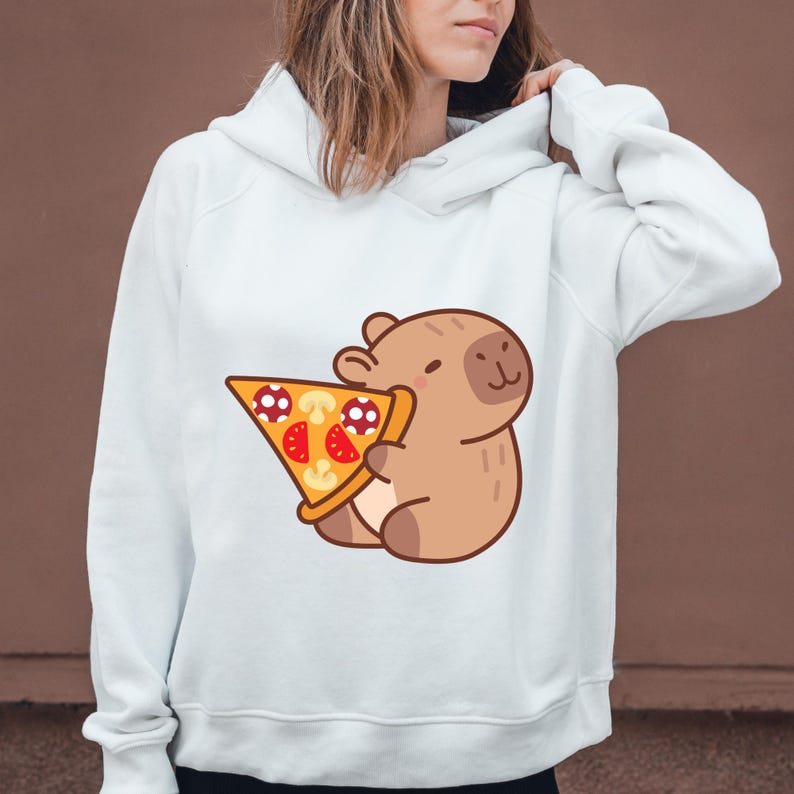 May include: White hoodie featuring a cartoon capybara holding a pizza slice. The pizza has red tomato slices, mushroom toppings, and a golden crust. The capybara is brown with a smiling face. The hoodie has a drawstring hood and long sleeves.