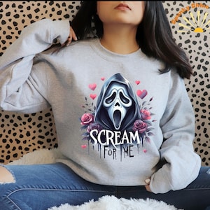 May include: A gray sweatshirt with a graphic print of the Ghostface character from the Scream movie franchise. The graphic includes a floral design and the text "Scream for Me".