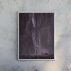 Peut inclure: Une photographie encadrée d'une cascade avec une personne debout devant elle. La cascade est d'un blanc brumeux et l'arrière-plan est d'un gris foncé.