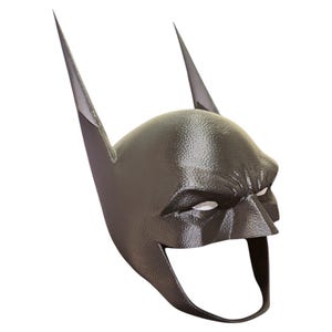 May include: A black plastic Batman mask with a pointed chin and two large, pointed ears. The mask has a textured surface and a white eye opening.