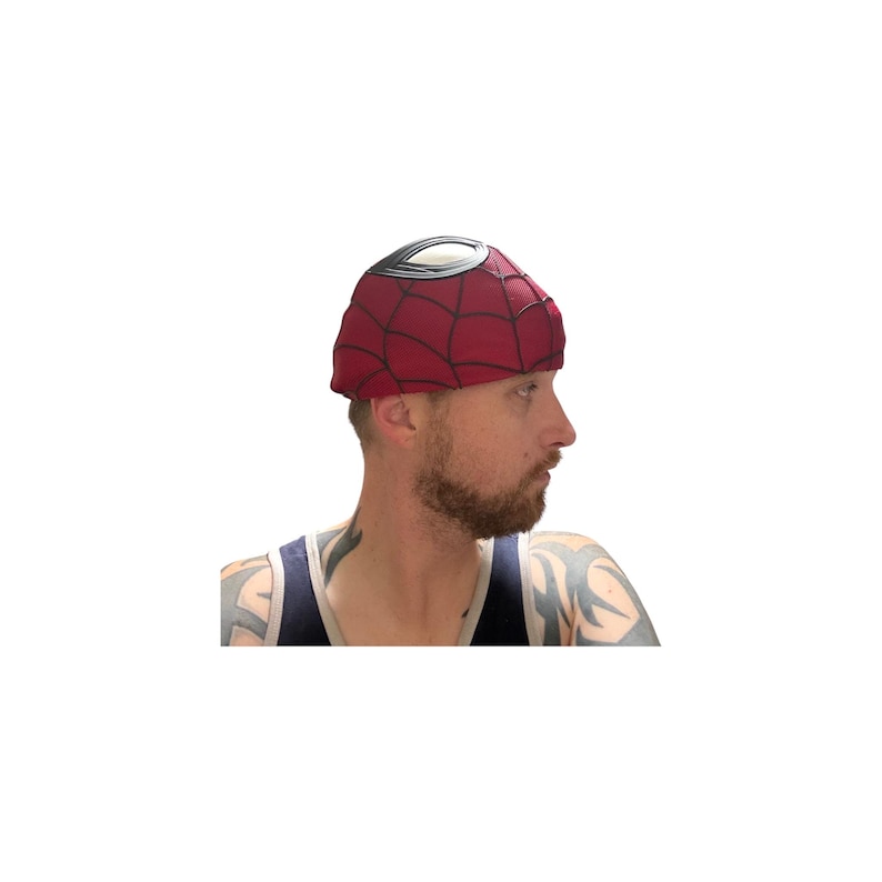 May include: A red beanie-style hat with a black web pattern and a white and black eye design. The hat is a costume accessory, likely inspired by a superhero. The hat is made of a soft material.