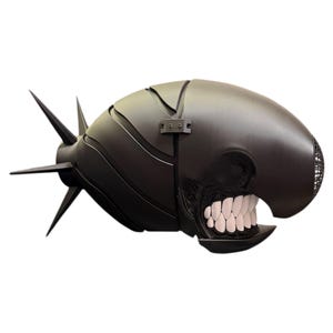 May include: A black, stylized sculpture resembling a torpedo or projectile with a menacing, open-mouthed design. The sculpture features sharp fins, a hinged section, and a detailed, toothy grin, creating a striking, dark aesthetic.
