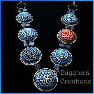 A necklace with seven different openwork polymer clay focal beads in blue and red colors.  This tutorial does not demonstrate how to color the openwork beads or how to assemble them into a necklace. This picture is to show the technique capabilities.