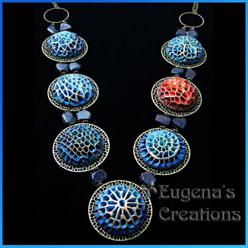A necklace with seven different openwork polymer clay focal beads in blue and red colors.  This tutorial does not demonstrate how to color the openwork beads or how to assemble them into a necklace. This picture is to show the technique capabilities.