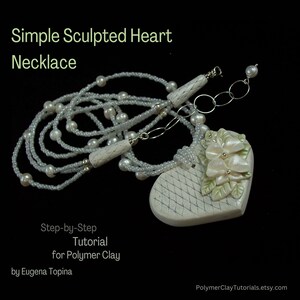 May include: A white polymer clay heart necklace with a delicate white bead chain and a floral design. The heart pendant has a textured surface and is accented with white flowers and green leaves. The necklace is titled "Simple Sculpted Heart Necklace" and includes the text "Step-by-Step Tutorial for Polymer Clay by Eugena Topina".