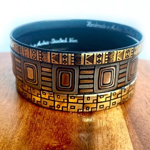 May include: Stacked decorative bowls with geometric patterns in gold, silver, and bronze tones. The bowls have a black interior and are displayed on a wooden surface. The text "Handmade in Australia" is visible.