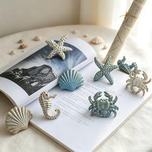May include: A collection of nautical-themed drawer knobs featuring various sea creatures including starfish, seahorses, crabs, and seashells. The hardware pieces are finished in shades of blue, white, and gold with a distressed, textured appearance.