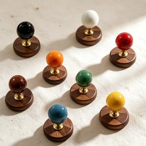 Puede incluir: Una colección de ocho pomos esféricos con bolas de cerámica brillante en colores negro, blanco, rojo, naranja, verde, marrón, amarillo y azul. Cada pomo está montado sobre una base circular de madera oscura con un conector de latón pulido.
