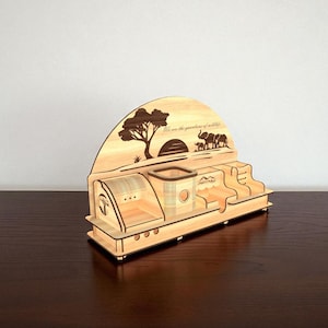 Puede incluir: Un organizador de escritorio de madera con tem&aacute;tica de vida silvestre. El organizador presenta dise&ntilde;os cortados con l&aacute;ser de un &aacute;rbol, elefantes y el texto "We are the guardians of wildlife". Tiene compartimentos para bol&iacute;grafos, notas y otros &uacute;tiles de oficina.
