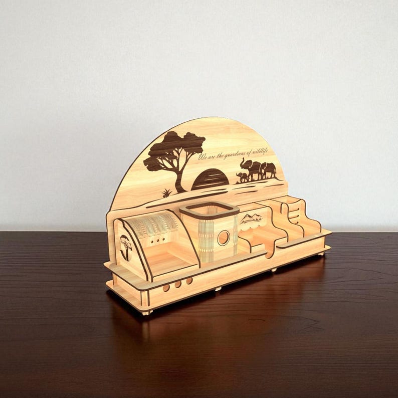 Puede incluir: Un organizador de escritorio de madera con tem&aacute;tica de vida silvestre. El organizador presenta dise&ntilde;os cortados con l&aacute;ser de un &aacute;rbol, elefantes y el texto "We are the guardians of wildlife". Tiene compartimentos para bol&iacute;grafos, notas y otros &uacute;tiles de oficina.