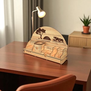 Puede incluir: Organizador de escritorio de madera con dise&ntilde;o tem&aacute;tico de la naturaleza. Presenta un &aacute;rbol, elefantes y el texto "We are the guardians of wildlife". Incluye compartimentos para bol&iacute;grafos, objetos peque&ntilde;os y un tel&eacute;fono. Madera clara.