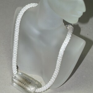 May include: A white beaded necklace with a clear glass pendant. The pendant is rectangular and has a silver-colored metal piece inside.