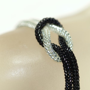May include: A black and silver beaded bracelet with a knot design.