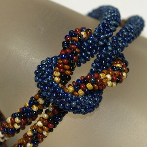 May include: A beaded bracelet with a knotted design. The bracelet is made with blue, red, white, and brown beads.