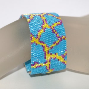 May include: A blue beaded bracelet with a yellow and purple geometric pattern.