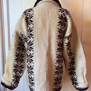 Puede incluir: Chaqueta de punto vintage color crema con tejido texturizado. Presenta cuello y ribetes azul marino oscuro, y patrones de copos de nieve en burdeos y azul marino a lo largo de las mangas y los laterales. Una prenda de abrigo c&aacute;lida y acogedora.