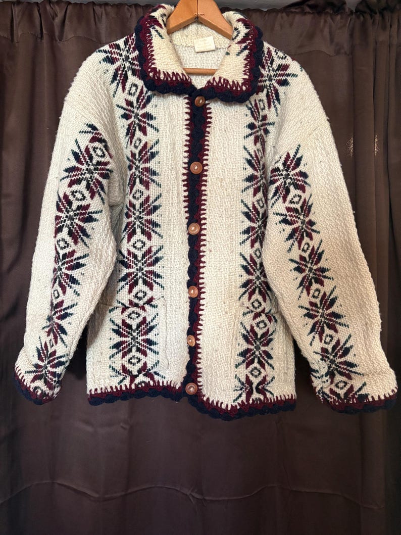 Puede incluir: C&aacute;rdigan color crema con botones y un estampado de copos de nieve en azul marino y burdeos. El su&eacute;ter tiene cuello chal y est&aacute; ribeteado en azul marino. Los botones son de color marr&oacute;n claro.