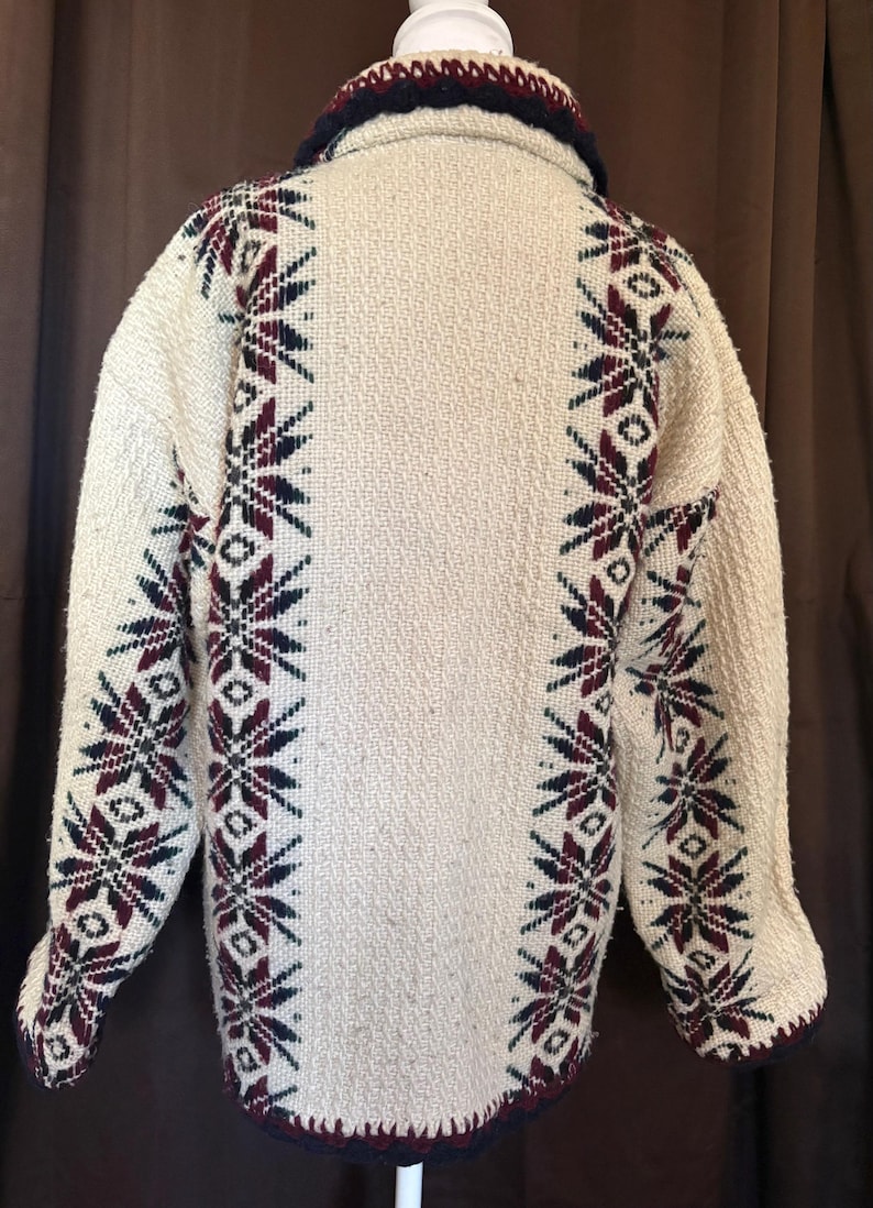 Puede incluir: Chaqueta tejida de color crema con cuello y ribete azul marino. La chaqueta presenta un patr&oacute;n repetido de dise&ntilde;os de copos de nieve burdeos y azul marino a lo largo de las mangas y los lados. La chaqueta tiene una apariencia texturizada.