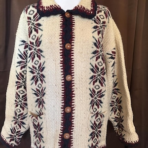 Puede incluir: C&aacute;rdigan color crema con botones y tejido texturizado. El su&eacute;ter presenta un cuello y ribete azul marino oscuro, con un patr&oacute;n de copo de nieve burdeos y azul marino. Tiene dos bolsillos y botones de madera.