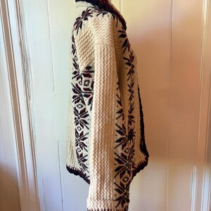 Puede incluir: C&aacute;rdigan de punto color crema con un estampado de copos de nieve en burdeos y azul marino. El su&eacute;ter tiene un tejido texturizado, cuello chal y pu&ntilde;os acanalados. Los bordes est&aacute;n ribeteados en azul marino y burdeos. El c&aacute;rdigan se exhibe en un maniqu&iacute;.