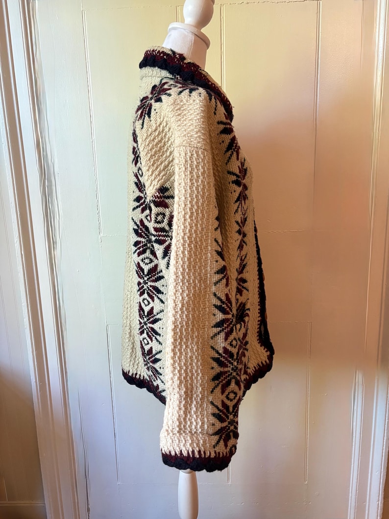 Puede incluir: C&aacute;rdigan de punto color crema con un estampado de copos de nieve en burdeos y azul marino. El su&eacute;ter tiene un tejido texturizado, cuello chal y pu&ntilde;os acanalados. Los bordes est&aacute;n ribeteados en azul marino y burdeos. El c&aacute;rdigan se exhibe en un maniqu&iacute;.