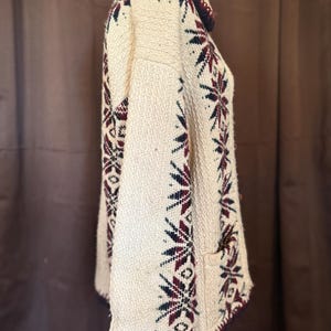 Puede incluir: Jersey de punto color crema con cuello alto y mangas largas. El jersey presenta un estampado de copos de nieve en azul marino, burdeos y verde. El cuello y los pu&ntilde;os est&aacute;n ribeteados con punto azul marino oscuro y burdeos.