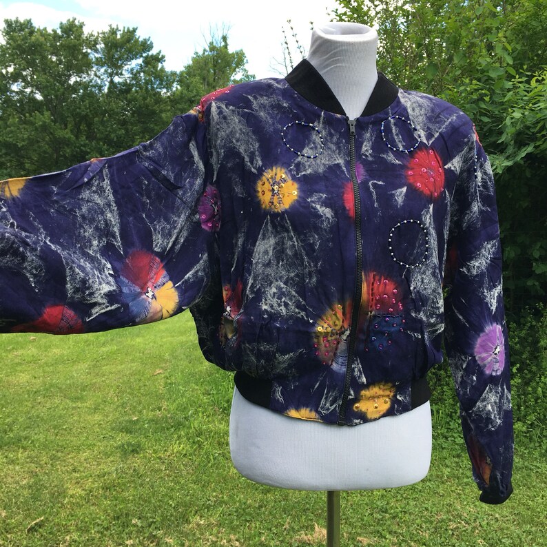 Puede incluir: Una chaqueta bomber morada con estampado tie-dye y lentejuelas de colores. La chaqueta tiene cierre de cremallera y dobladillo y pu&ntilde;os de canal&eacute;.